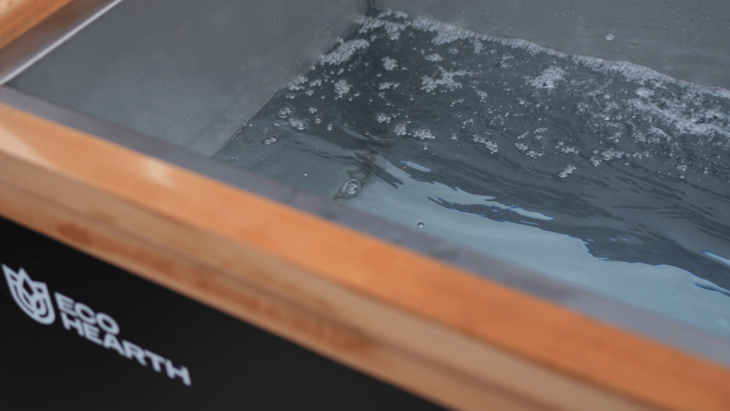 Close-up view of Eco Hearth cold plunge tub filled with chilled bubbling water, stainless steel interior and wooden edge visible