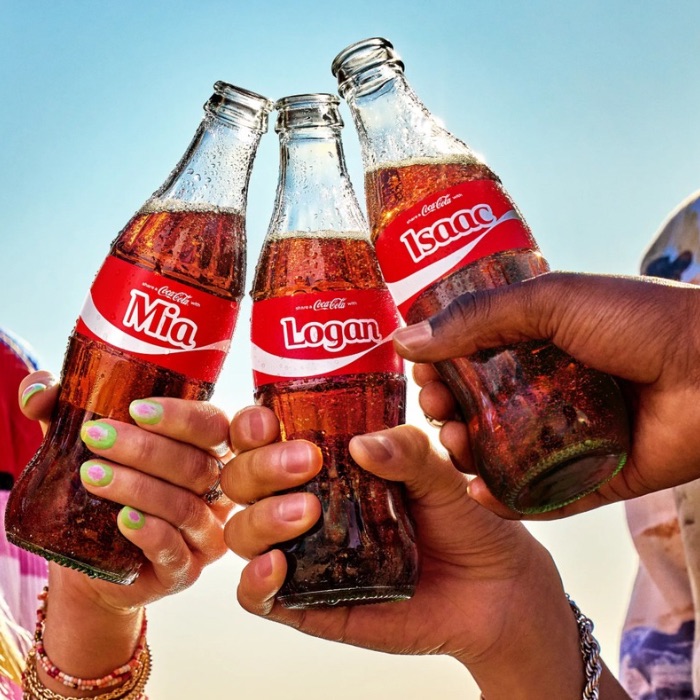 People holding personalized Coca-Cola bottles labeled Mia, Logan, and Isaac, celebrating the Share a Coke campaign.