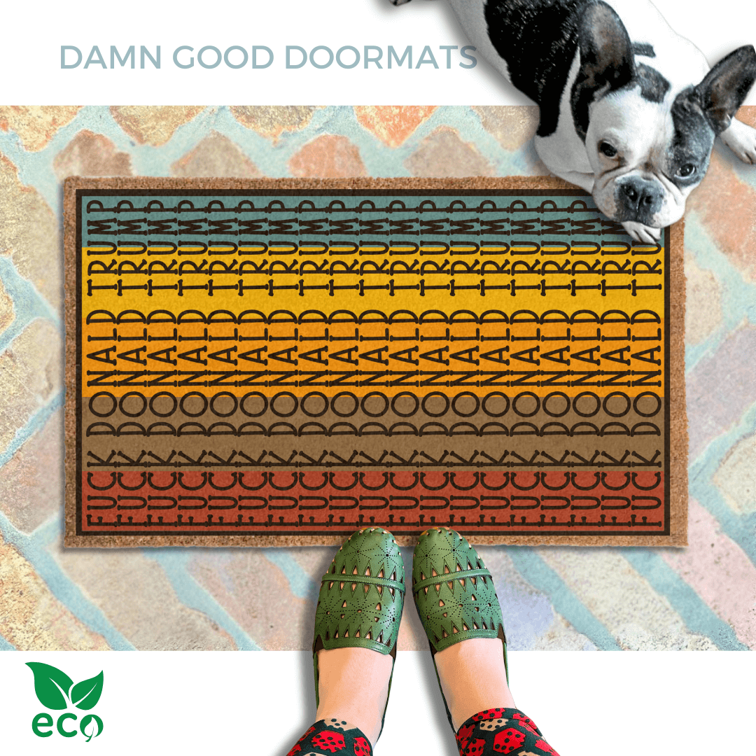 A pair of feet wearing green shoes stands on a subtle colorful, patterned FDT Fuck Donald Trump doormat, with a french bulldog sitting on the floor next to them.