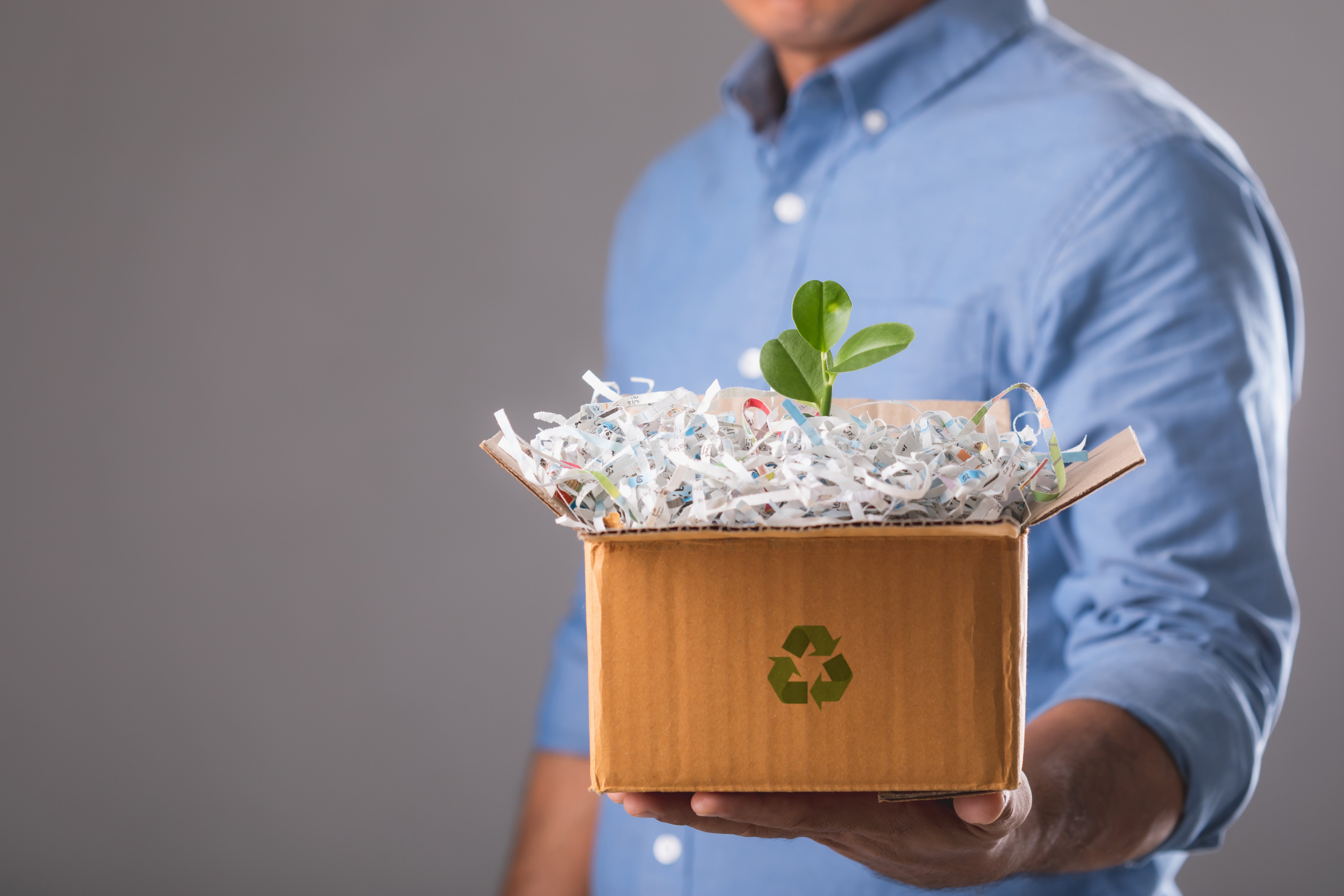 Man holding a box with recycle sign on it, filled with crushed paper and some leaves