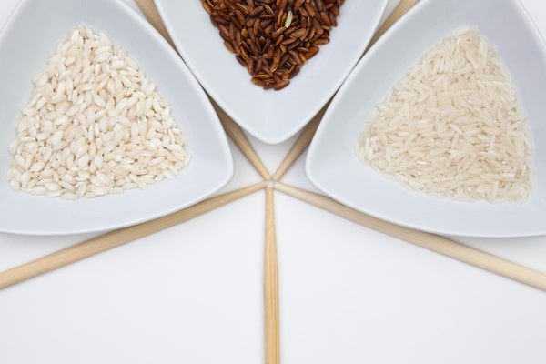 5 Keto Rice Substitutes With Fewer Than 5 Net Carbs 2 An overhead view shows three white, triangular bowls arranged in a star shape and filled with different types of uncooked rice.