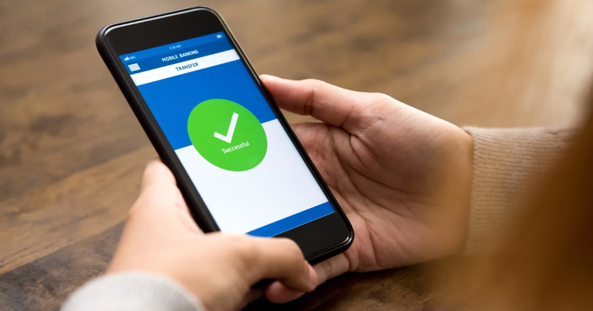 Person holding a smartphone showing a successful money transfer confirmation screen.