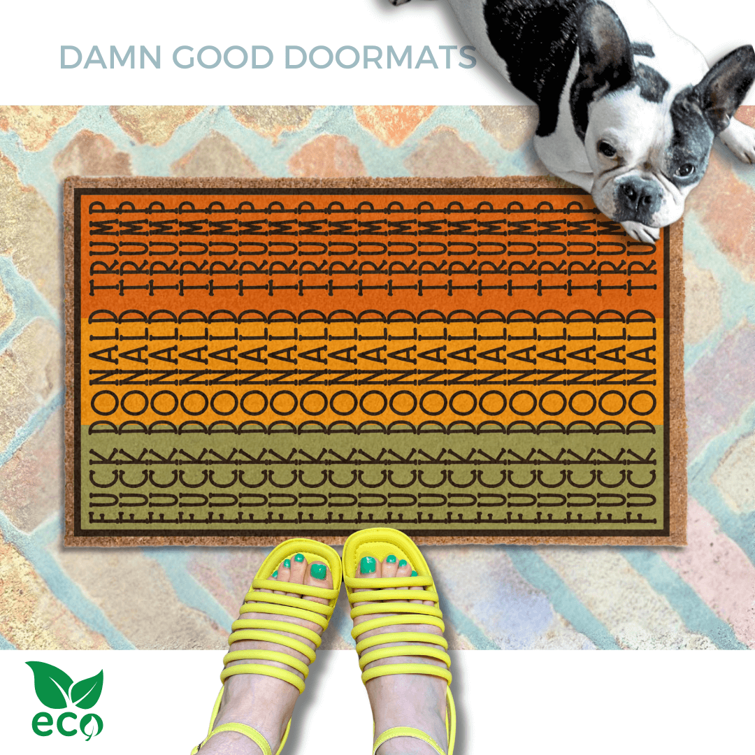a pair of feet in yellow strappy sandals standing on an all-weather tri-color, patterned doormat with a geometric Fuck Donald Trump design and a french bulldog looking up.