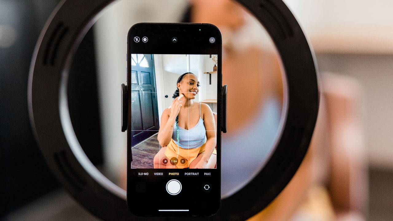 Woman filming a vertical YouTube Shorts video using a smartphone and ring light, captured through the phone screen during a content creation session. Woman filming a vertical YouTube Shorts video using a smartphone and ring light, captured through the phone screen during a content creation session.