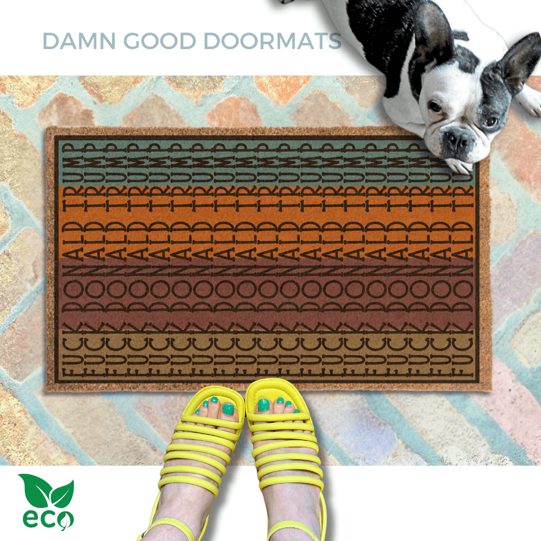 a pair of feet in yellow strappy sandals standing on an all-weather Fall door mat colorful, patterned doormat with a geometric Fuck Donald Trump design and a french bulldog looking up.